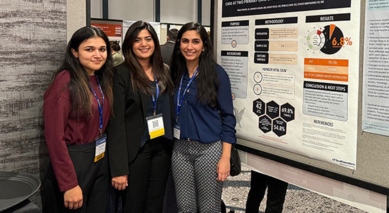 Three women pose in front research posters at a conference