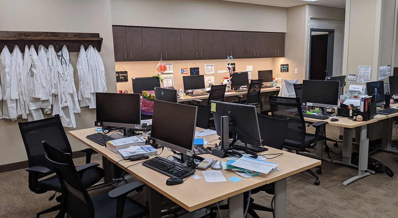 A room filled with computer workstations on tables, with white medical coats hanging on the wall