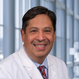 Dr. David Aguilar wearing a white coat, light blue shirt with a striped tie standing in the Clements Unirversity Hospital