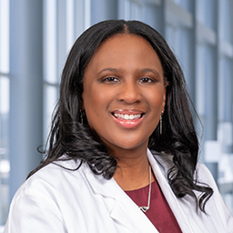 Dr. Nicole Johnson wearing a maroon shirt and a white lab coat standing in the Clements University Hospital lobby