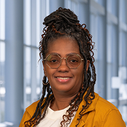 Libby Burks wearing octagonal glasses and a yellow jacket, standing in the Clements University Hospital lobby