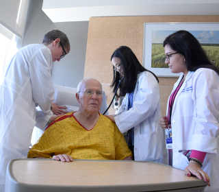 an attending doctor and medical students gathered around an elderly patient in a hospital room