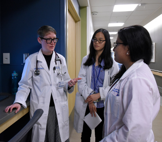 an attending doctor and medical students gathered around an elderly patient in a hospital room