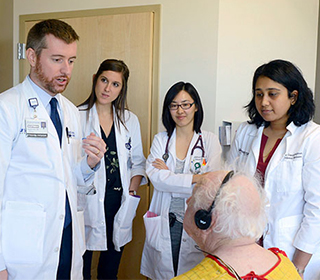 an attending doctor and medical students gathered around an elderly patient in a hospital room