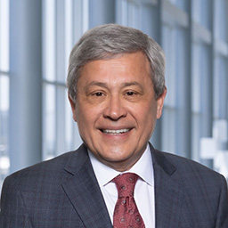 Dr. Carlos Arteaga wearing a dark suit with a white shirt and and red tie standing in the Clements University Hospital lobby