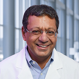 Dr. Robert Bachoo wearing a blue shirt and a white lab coat standing in the Clements University Hospital lobby