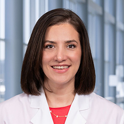 Dr. Victoria Chung wearing a bright red shirt and a white lab coat standing in the Clements University Hospital lobby