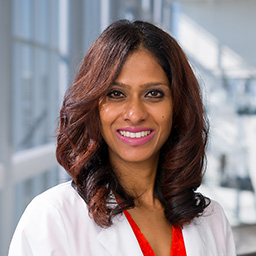 Dr. Poorni Manohar wearing a red shirt and a white lab coat standing in the Clements University Hospital lobby