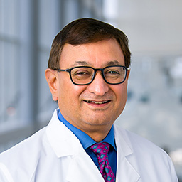 Dr. Ravindra Sarode wearing a bright blue shirt with a patterned and a white lab coat standing in the Clements University Hospital lobby