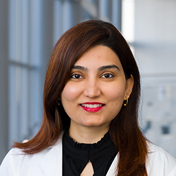 Dr. Nawal Shaikh wearing a black shirt and a white lab coat standing in the Clements University Hospital lobby