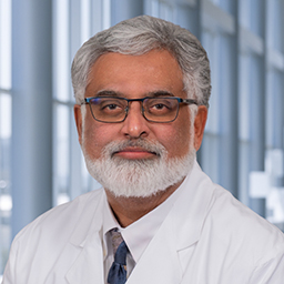 Dr. Amir Toor wearing a white shirt with a blue and grey tie and a white lab coat standing in the Clements University Hospital