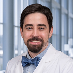 Dr. Joseph Vento wearing a light blue shirt with a blue bow tie and a white lab coat standing in the Clements University Hospital lobby