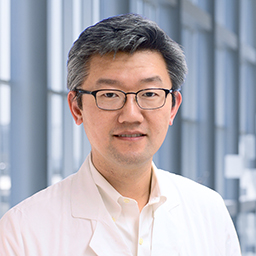 Dr. Hao Zhu wearing a white shirt and a white lab coat standing in the Clements University Hospital lobby