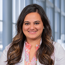 Dr. Sanah Ladhani wearing a floral print shirt with a white lab coat standing in the Clements University Hospital lobby