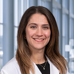 Dr. Brianna Saadat  wearing  a black shirt, and a white lab coat standing in the Clements University Hospital lobby