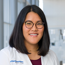 Dr. Amanda Zhang wearing glasses, a maroon shirt, and a white lab coat standing in the Clements University Hospital lobby