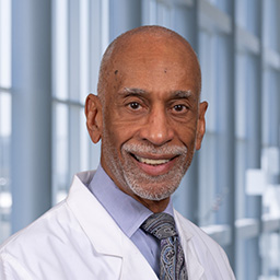 Dr. Donald Wesson wearing a white coat and light blue shirt with a gray patterned tie standing in the Clements University Hospital lobby