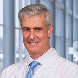 Dr. Joseph Crossno wearing a white lab coat, white shirt and a light blue tie standing in the CUH lobby