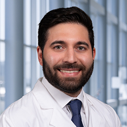 Dr. Adnan Khan wearing a white lab coat, white shirt and a dark blue tie, standing in the CUH lobby