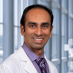 Dr. Govind Krishnan wearing a white lab coat, purple shirt and a purple stripped tie, standing in the CUH lobby