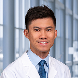 Dr. Henry Boyi Han wearing a white lab coat, light blue shirt and patterned blue tie standing in the CUH lobby