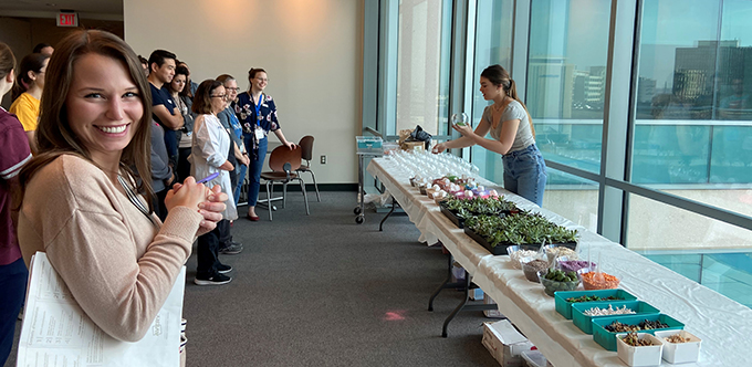 People lined up in front of a table containing materials for making a succulent planter