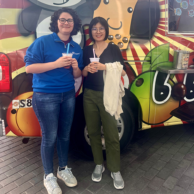 Two people pose for the camera in front of a smoothie truck