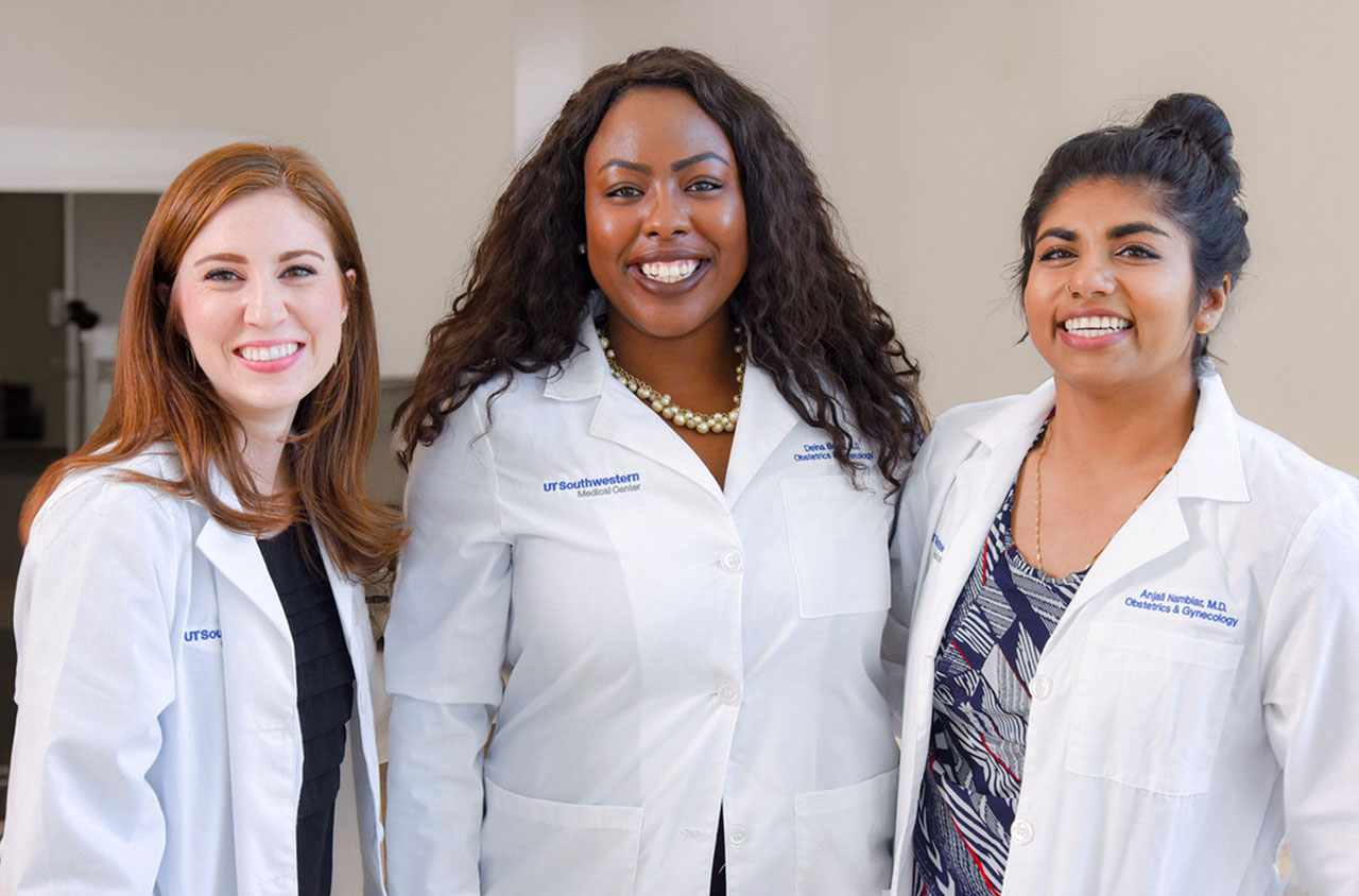 Three young women in white coats smiling at the camera