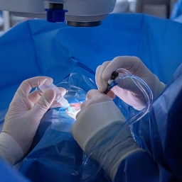 A pair of hands with white gloves operating as the gloved left hand of another person holds a dropper at the operation site.