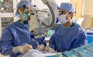 Two men in full surgical scrubs, looking into a scope while performing surgery.