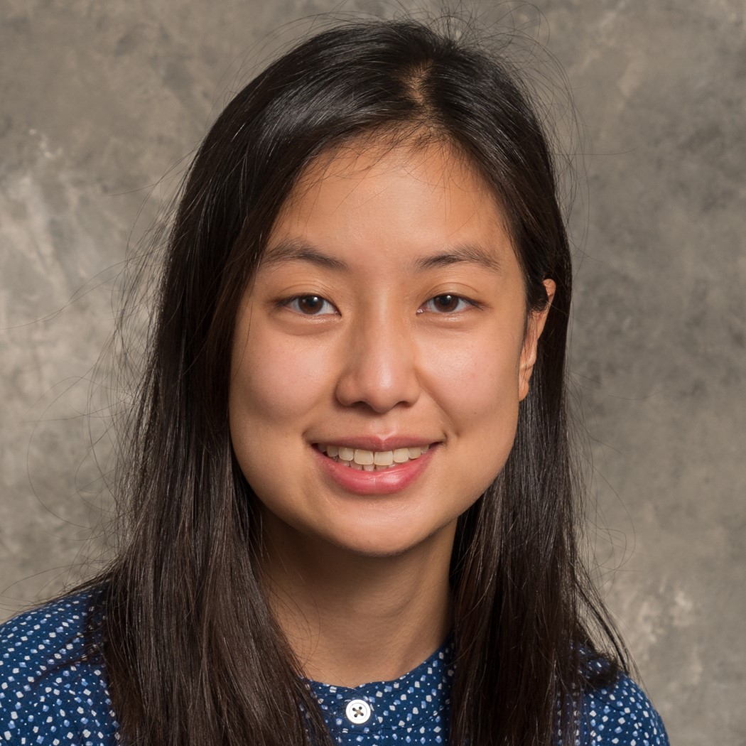 Smiling young woman with long black hair, wearing a blue and white patterned top.