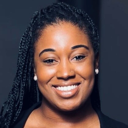 Smiling young woman with long black braided hair wearing a black blouse and pearl earrings