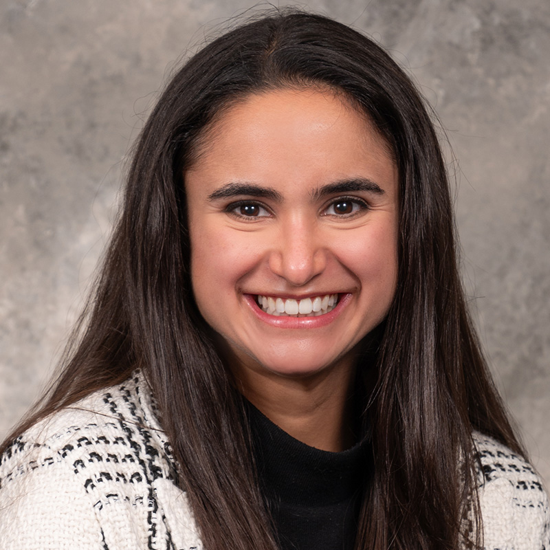 Smiling woman with long dark hair wearing a black and white patterned jacket.