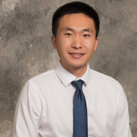 Smiling young man with short dark hair, wearing a white dress shirt and blue tie.