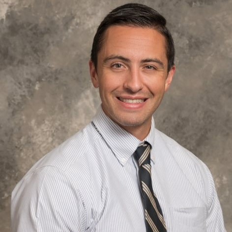 Smiling young man with short brown hair, wearing light-colored striped shirt and a dark striped tie.