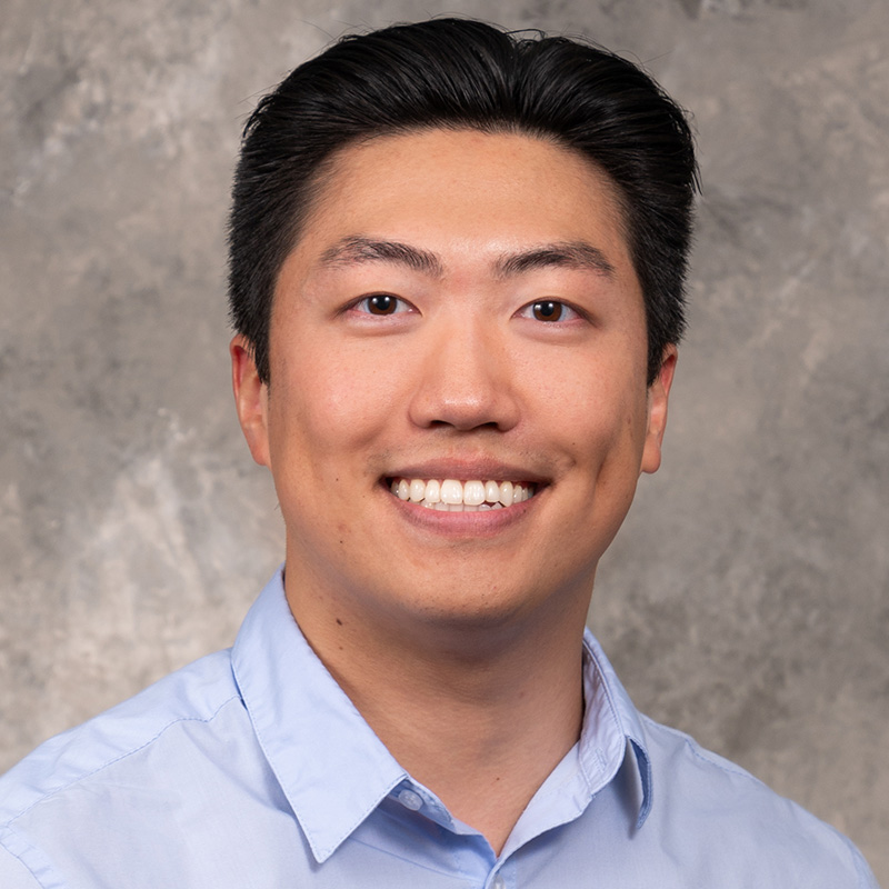 Smiling man with black hair, wearing a powder blue dress shirt.