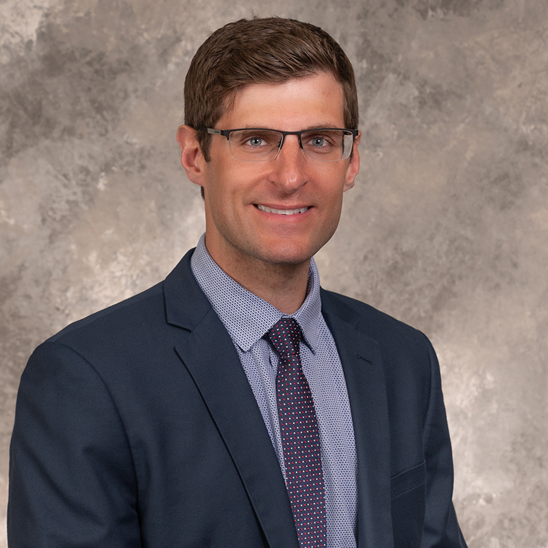 Smiling man with short brown hair wearing light-rimmed glasses, wearing a white lab coat and shirt.