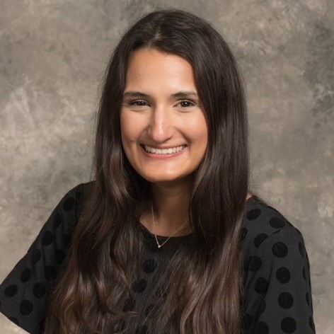 Smiling young woman with long dark hair, wearing a black-on-black polka dot top.