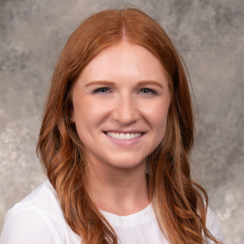 Smiling woman with long red hair, wearing a white top.