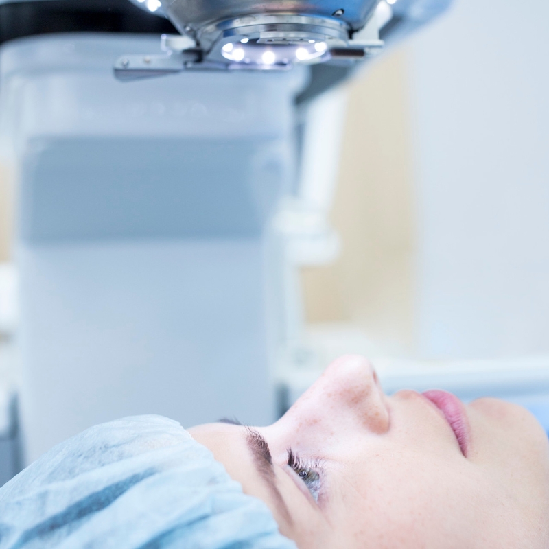 Female patient with blue hair cap on operating table looking up at laser