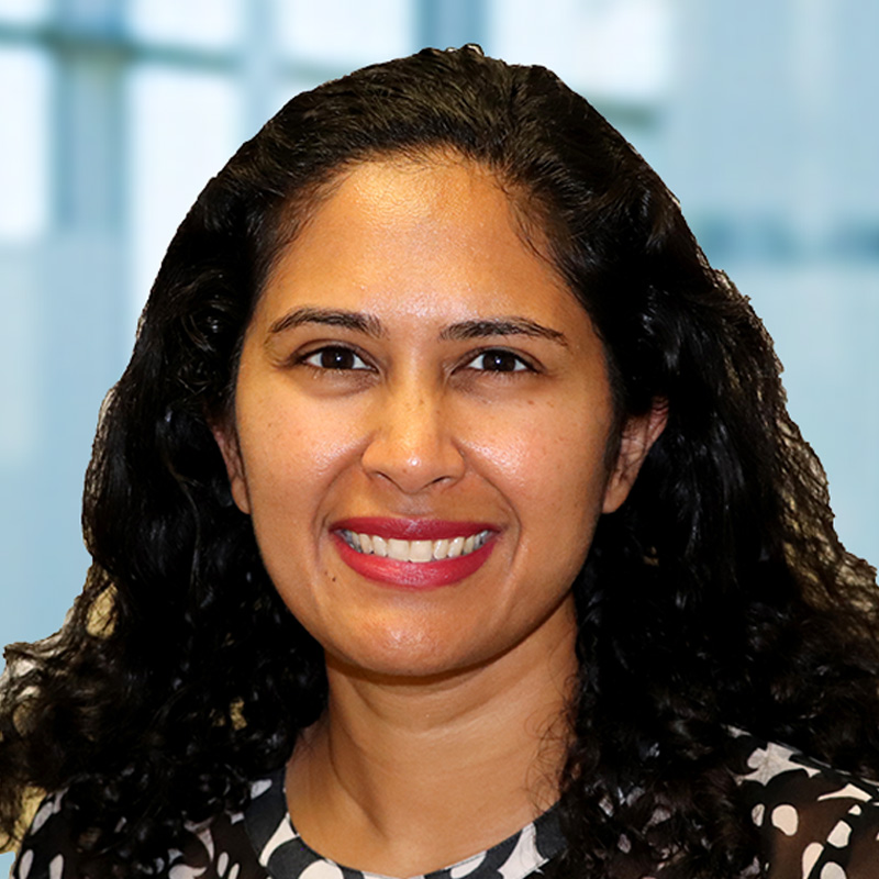 Smiling woman with curly black shoulder-length hair wearting a multi-colored blouse.