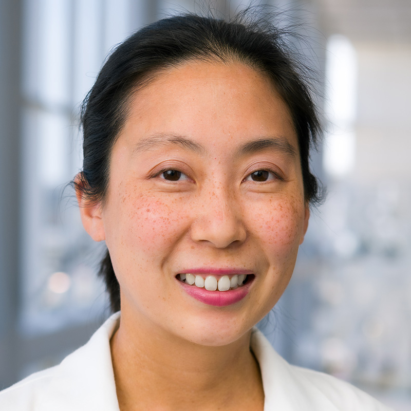 Smiling woman with black hair pulled back in a ponytail wearing a cream blouse and a white lab coat