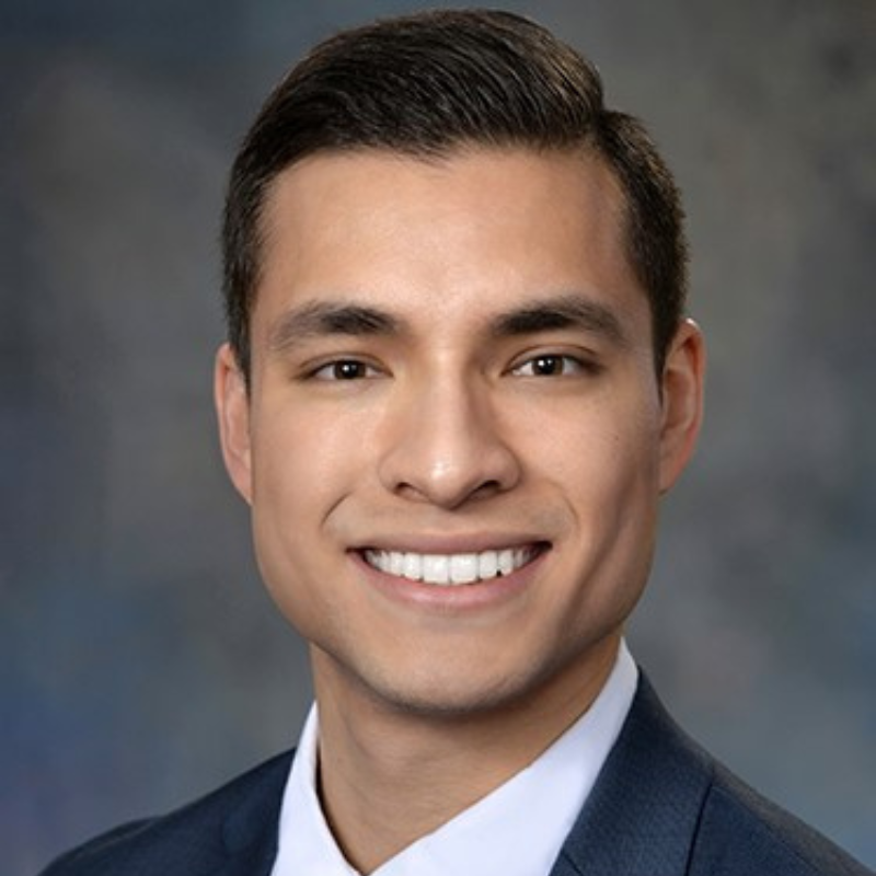 Smiling man with black hair wearing a white dress shirt and dark blue suit coat.