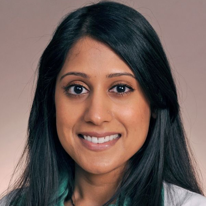 Smiling woman with long black hair wearing a kelly green blouse and white lab coat.