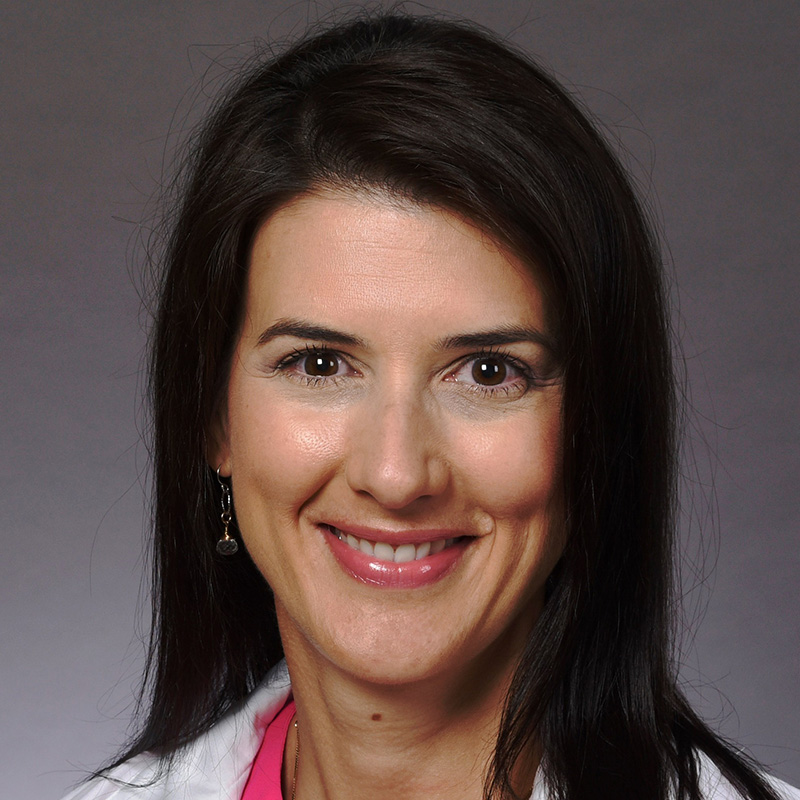 Smiling woman with brown shoulder-length hair wearing a hot pink blouse and white lab coat.