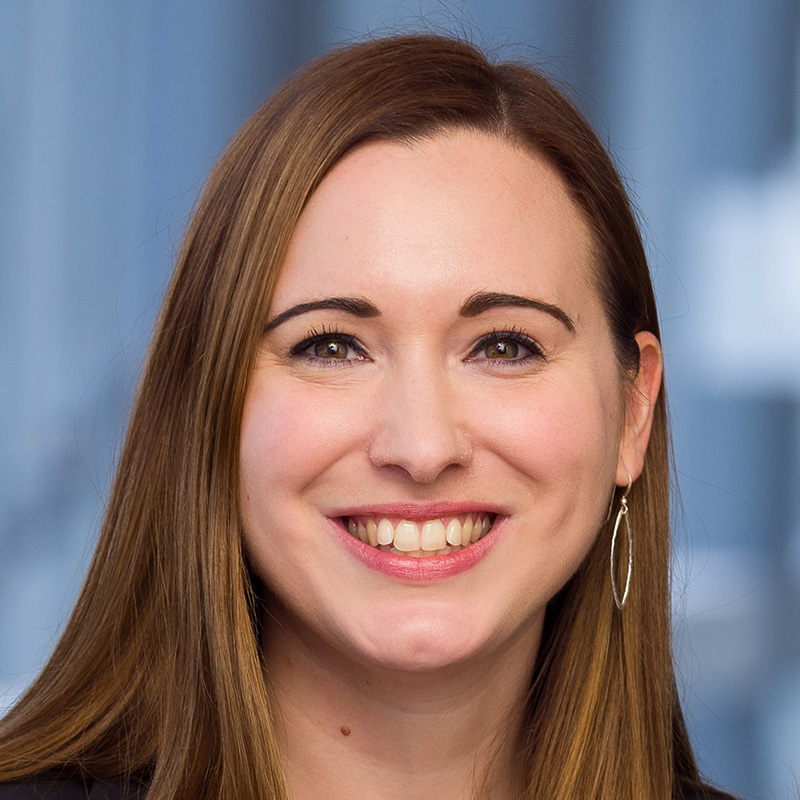 Smiling woman with long brown hair wearing a cobalt blue blouse and black blazer.