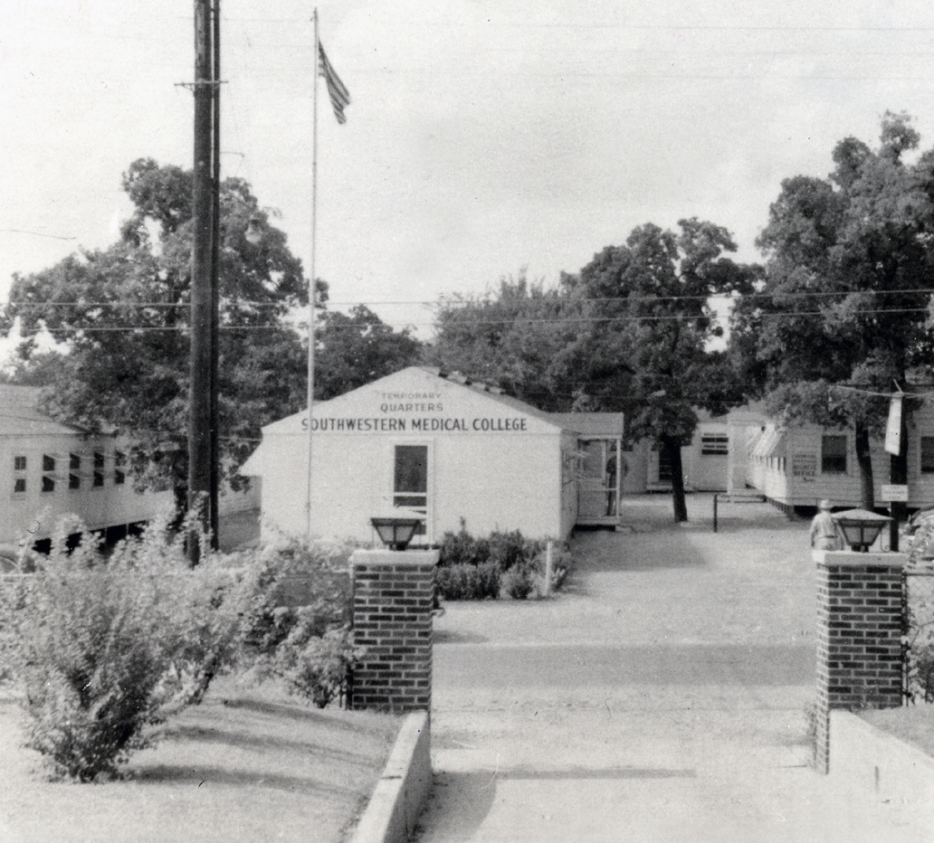 UTSW Medical School 1943 single story building in center of walkway with shrubs and flagpole at left