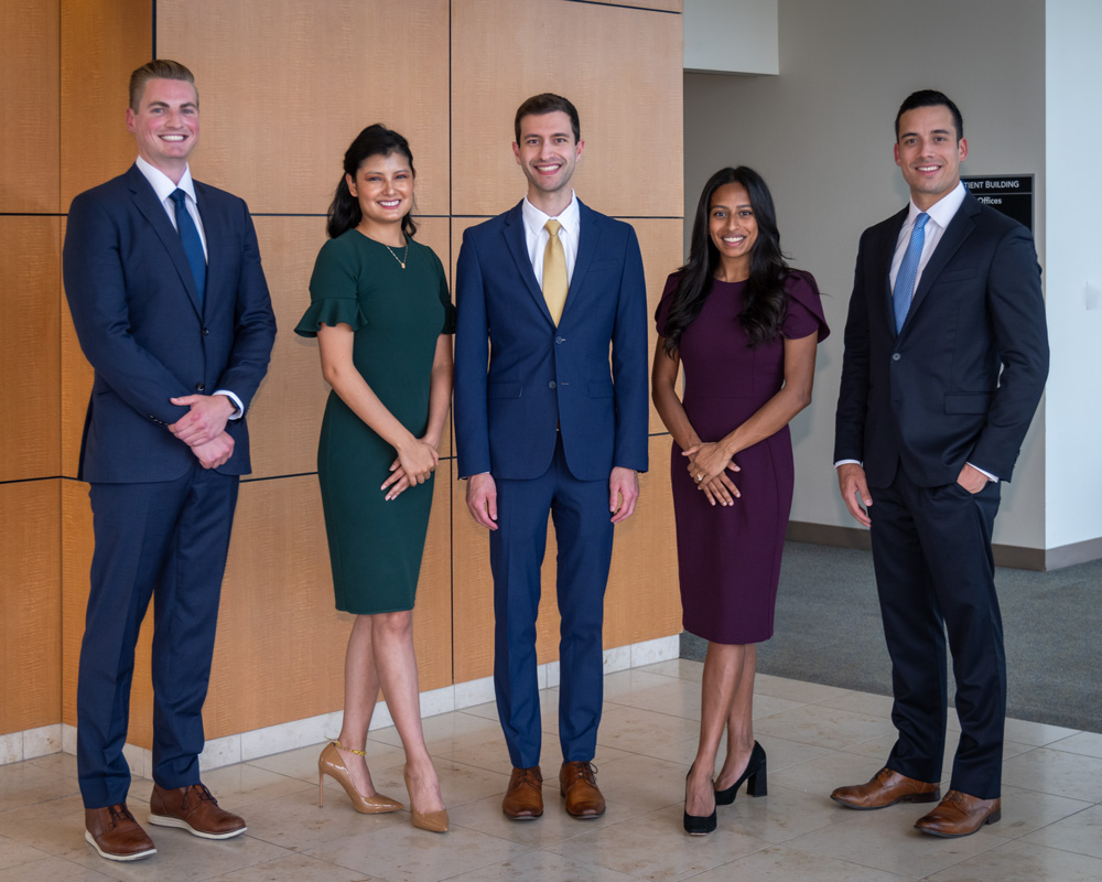 Three men wearing suits and two women wearing dresses, smiling, standing in front of a wood paneled wall.