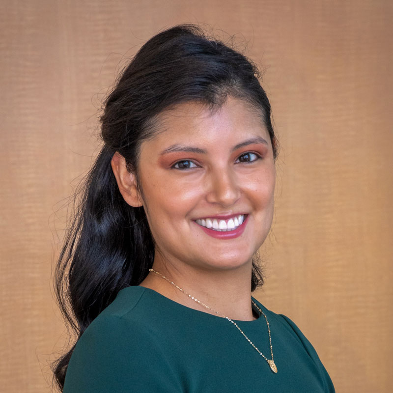 Smiling woman with long dark hair, wearing a green dress and a pendant necklace.