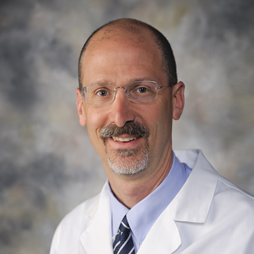 Dr. Kane, a smiling man with sandy hair and mustache, and a white beard, wearing a lab coat and glasses.